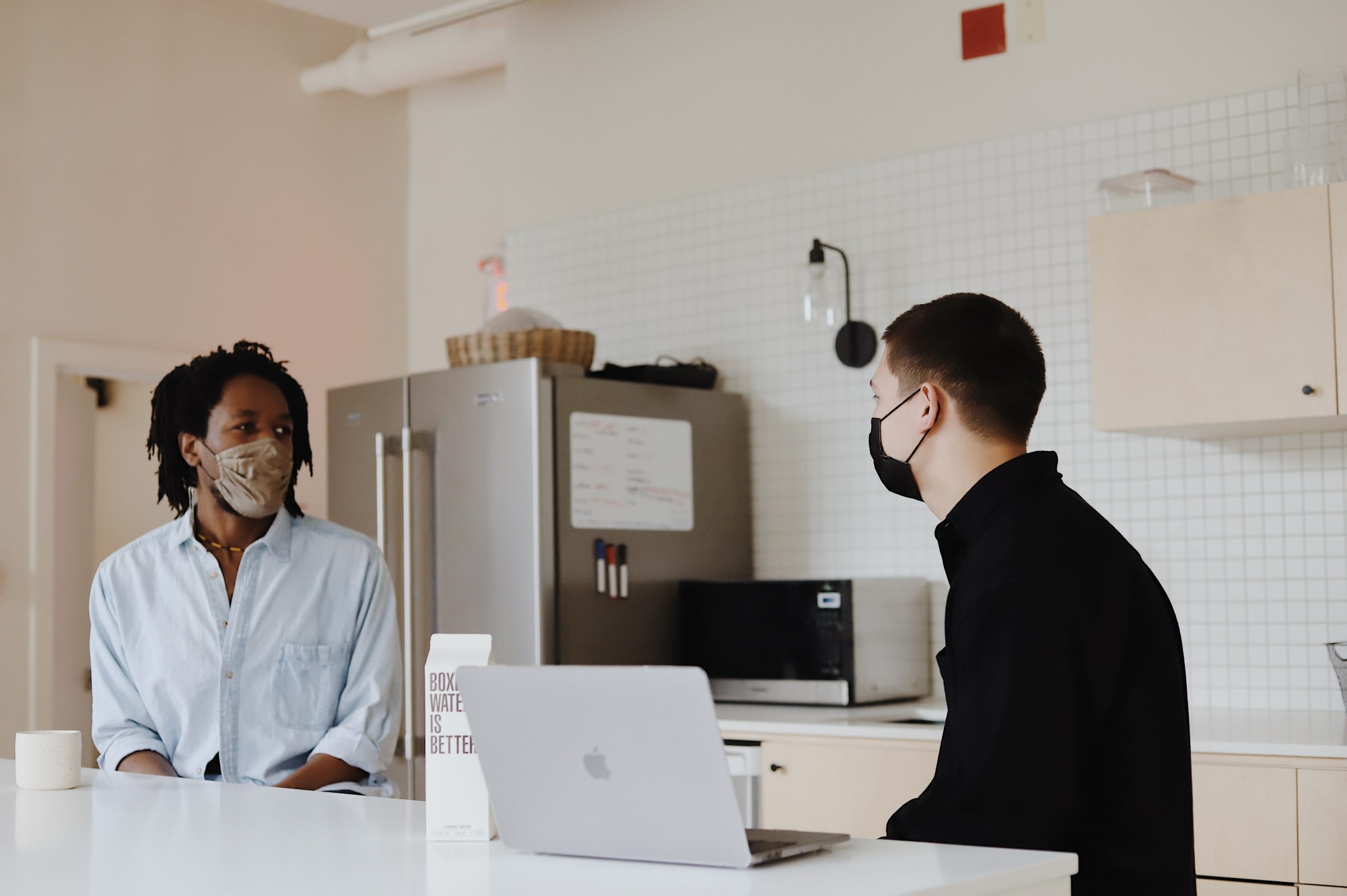 Men wearing face mask having a conversation in front of a computer